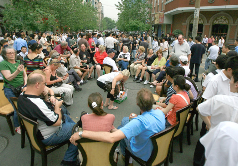 Image: Tourists sits in the street after they were evacuated from the Sichuan Hotel following a major earthquake