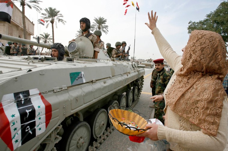 Image: A resident throws sweets towards Iraqi soldiers on a tank during a handover ceremony in Basra
