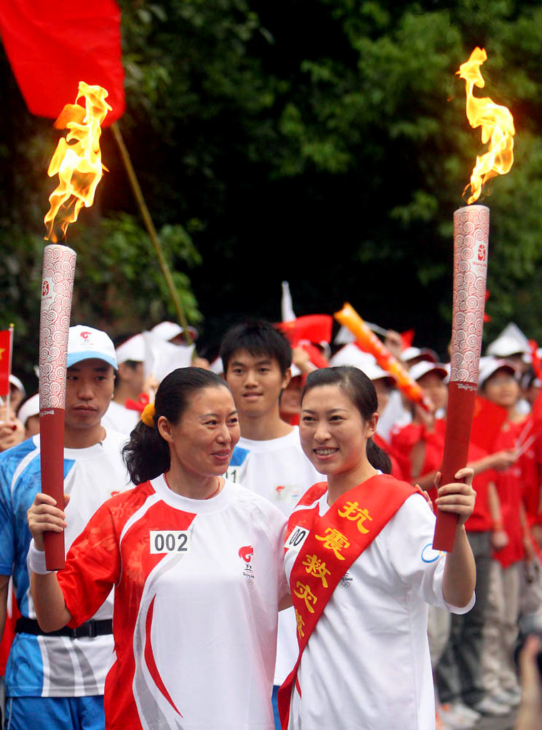 In this photo distributed by the official Chinese news agency Xinhua, torchbearer Jiang Min, right, displays the torch with the next torchbearer Jiao Shihua during the Beijing 2008 Olympic Games torch relay Sunday.