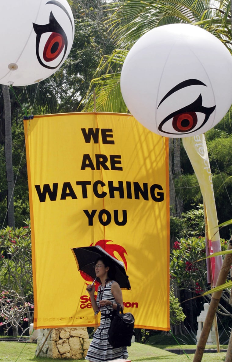 A delegate to the U.N. climate conference walks past a sign put up by an environmental activist group Wednesday Dec. 12, 2007, in Nusa Dua, Bali, Indonesia. As the high level ministerial meetings began, the U.N. chief said Wednesday that guidelines on greenhouse gas emissions cuts opposed by the United States may be