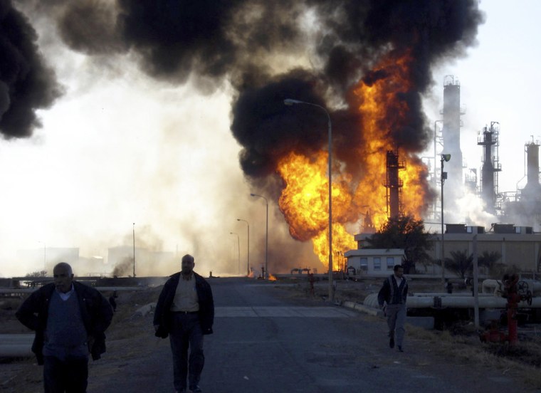 Workers walk away from a fire that broke out at the oil refinery in Baiji