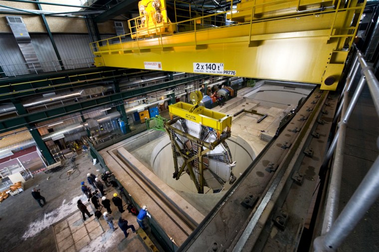 As workers look on, a 100-ton wheel is lowered Friday into the cavern containing the ATLAS particle detector at the Large Hadron Collider. The wheel is part of an apparatus that will detect muons given off by proton collisions in ATLAS.