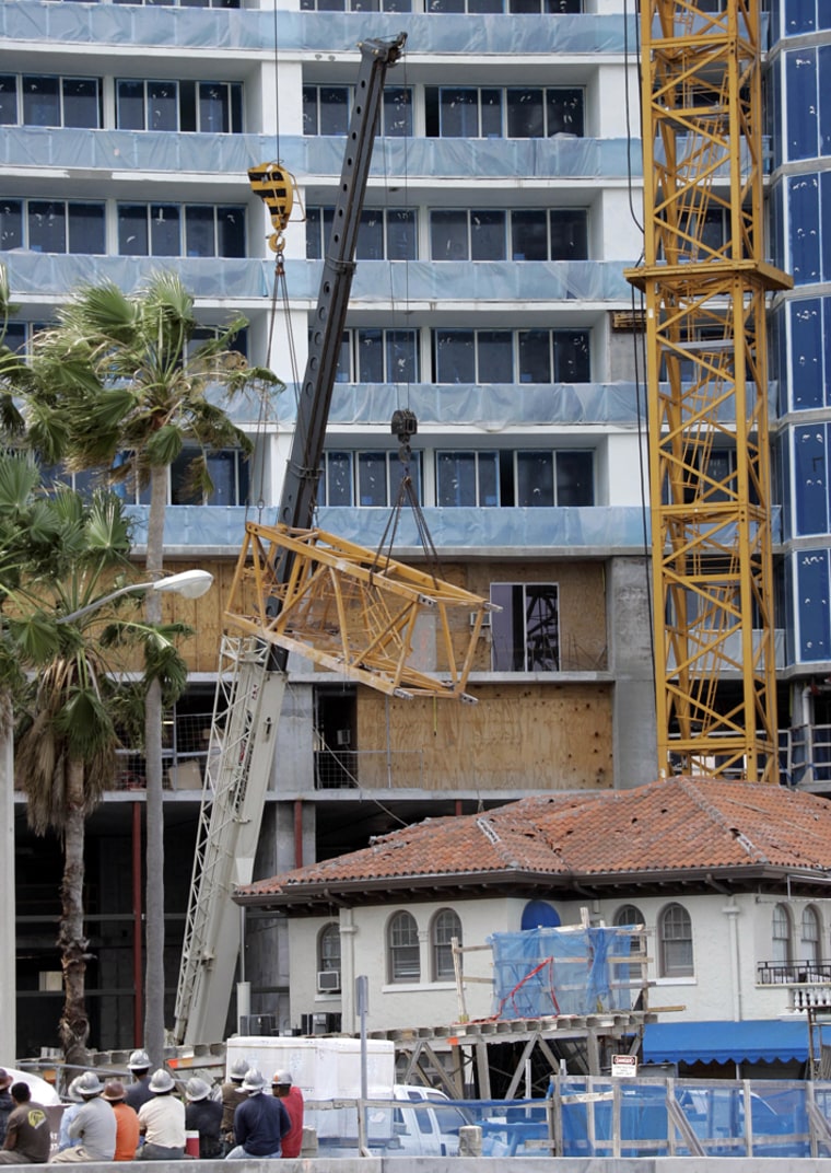 Image: Construction workers look on as a section of a crane is lifted from a house and set on the ground