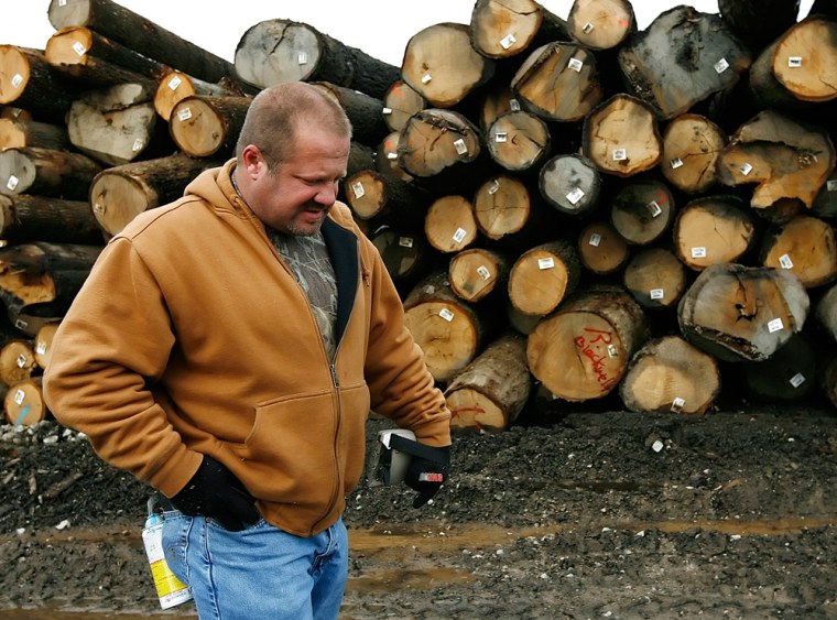 Image: Man walks by a stack of logs