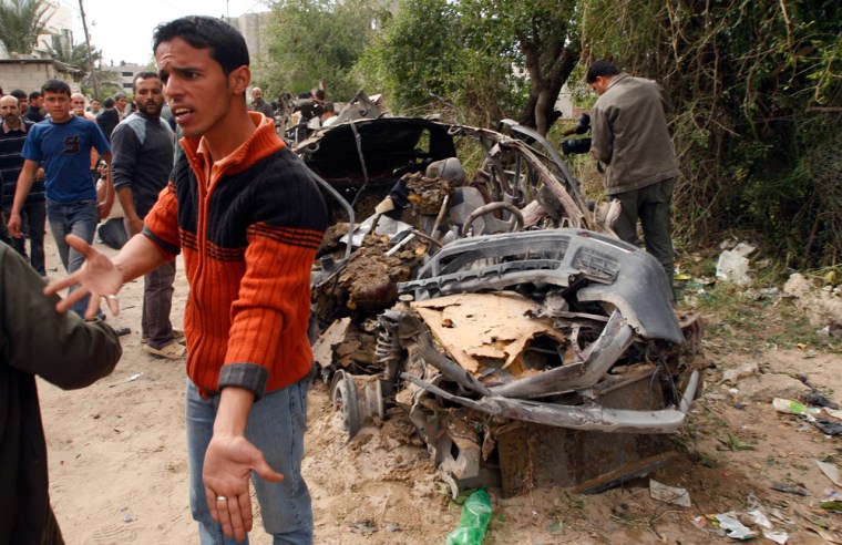 Image: A Palestinian man reacts next to a destroyed car.