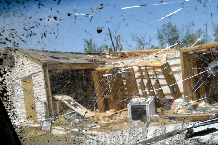 Image: A tornado damaged home is seen through a cracked windshield of a truck