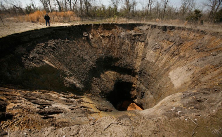 John Sparkman is dwarfed as he looks into a sinkhole near Picher, Okla., Saturday, April 6, 2008. Years of lead and zinc mining has left turned the town into a superfund site with sinkholes, lead-laced mountains of rock, and tainted water.  (AP Photo/Charlie Riedel)