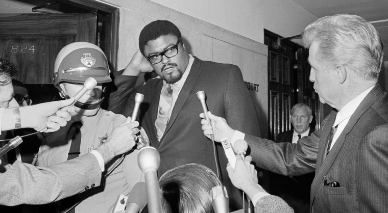 Roosevelt Grier, former defensive lineman for the Los Angeles Rams, towers over newsmen seeking to interview him February 17, 1969 after he testified for the prosecution in the trial of Sirhan Sirhan, accused of slaying Sen. Robert F. Kennedy. Grier told how he wrestled the gun from Sirhan in the chaotic moments after Kennedy was shot. (AP Photo)