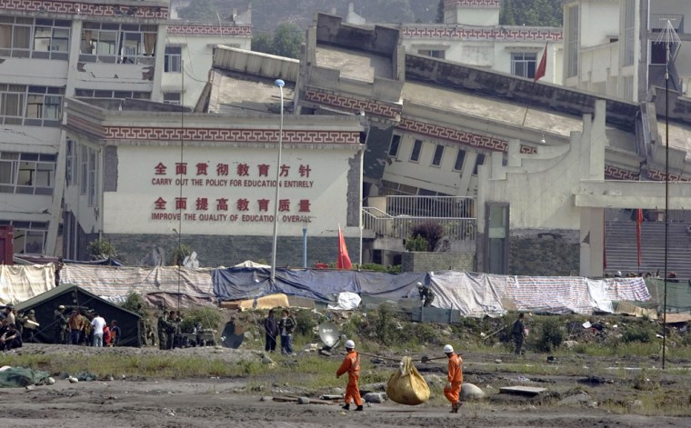 Rescue workers carry supplies past the main building of a school devastated by the May earthquake in Yingxiu in southwestern China's Sichuan province. The Chinese government said it would investigate why so many school buildings collapsed in the quake. 