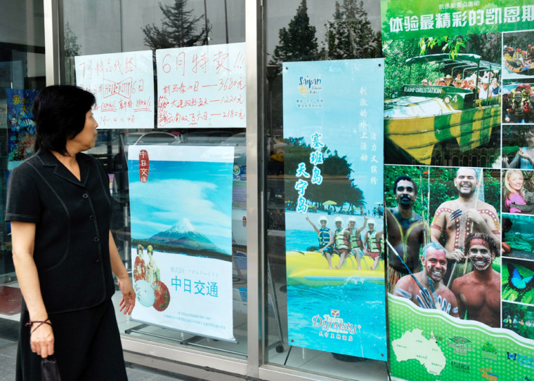 Image: A pedestrian looks at travel promotion posters on display in front of a travel agency in Beijing