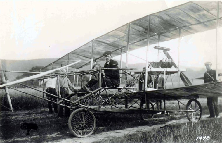 In this photo provided by the Glenn H. Curtiss Museum, Glenn H. Curtiss is seen seated in the June Bug just before take off, circa July 4, 1908 in Hammondsport, N.Y.  On a steamy Fourth of July evening a century ago, a wood-and-fabric biplane lifted off from Stony Brook Farm and stayed airborne for almost a mile in a stupendous triumph over gravity witnessed by more than 2,000 people.  (AP Photo/Glenn H. Curtiss Museum) **NO SALES**