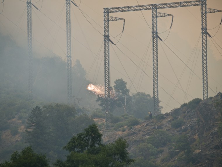 Sparks fly off powerlines engulfed by smoke from a wildfire north of Sacramento on Monday. Powerlines in parts of California are threatened not only by the fires but by a heat wave testing the grid's ability to deliver.