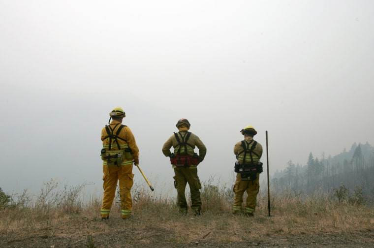Image: Firefighters Matt Nelson, left, Capt. Troy Doehier, center and Shawn Wolf, right, from the Sacramento Fire Department, stare out into the smoke, from the Butte Lightening Complex Fire