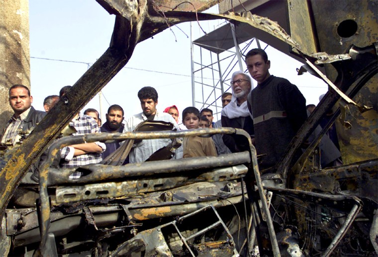 IRAQIS LOOK AT CAR DAMAGED IN AN EXPLOSION OUTSIDE A MOSQUE IN BAGHDAD