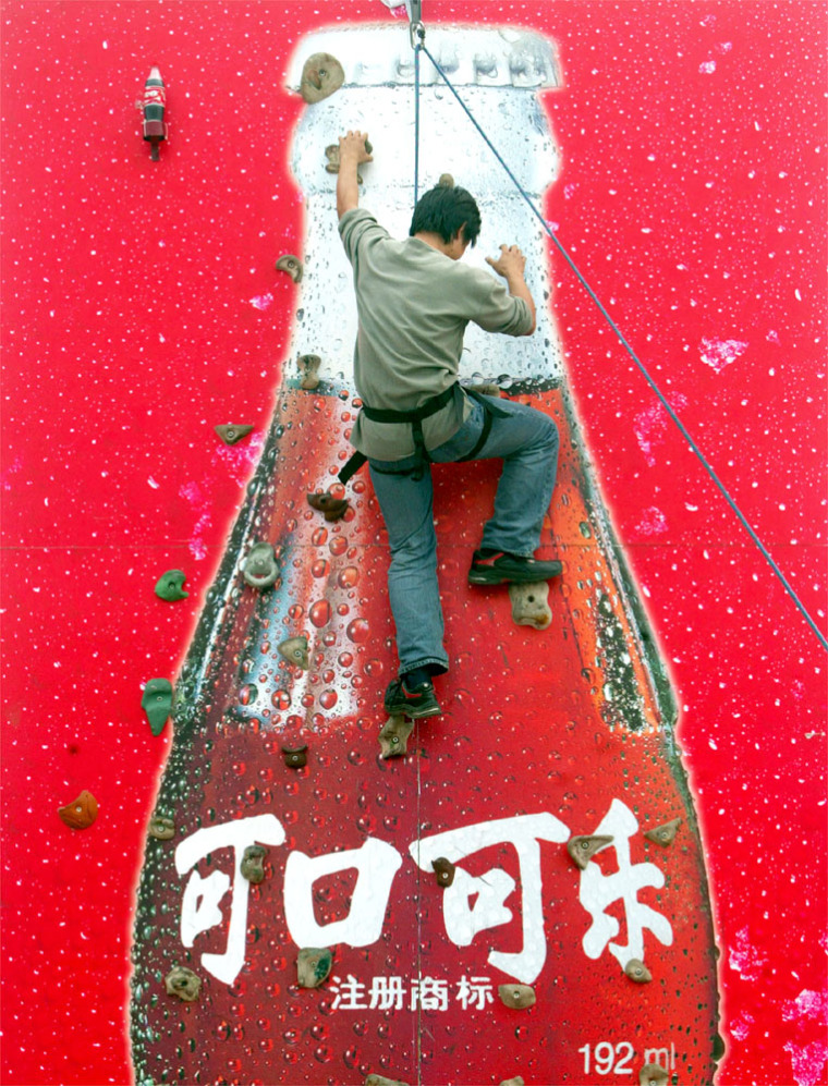 A CHINESE MAN CLIMBS ON A COKE ADVERTISEMENT TO ATTRACT CUSTOMERS AT THE FIRST CHINA INTERNATIONAL BEVERAGE FESTIVAL IN BEIJING