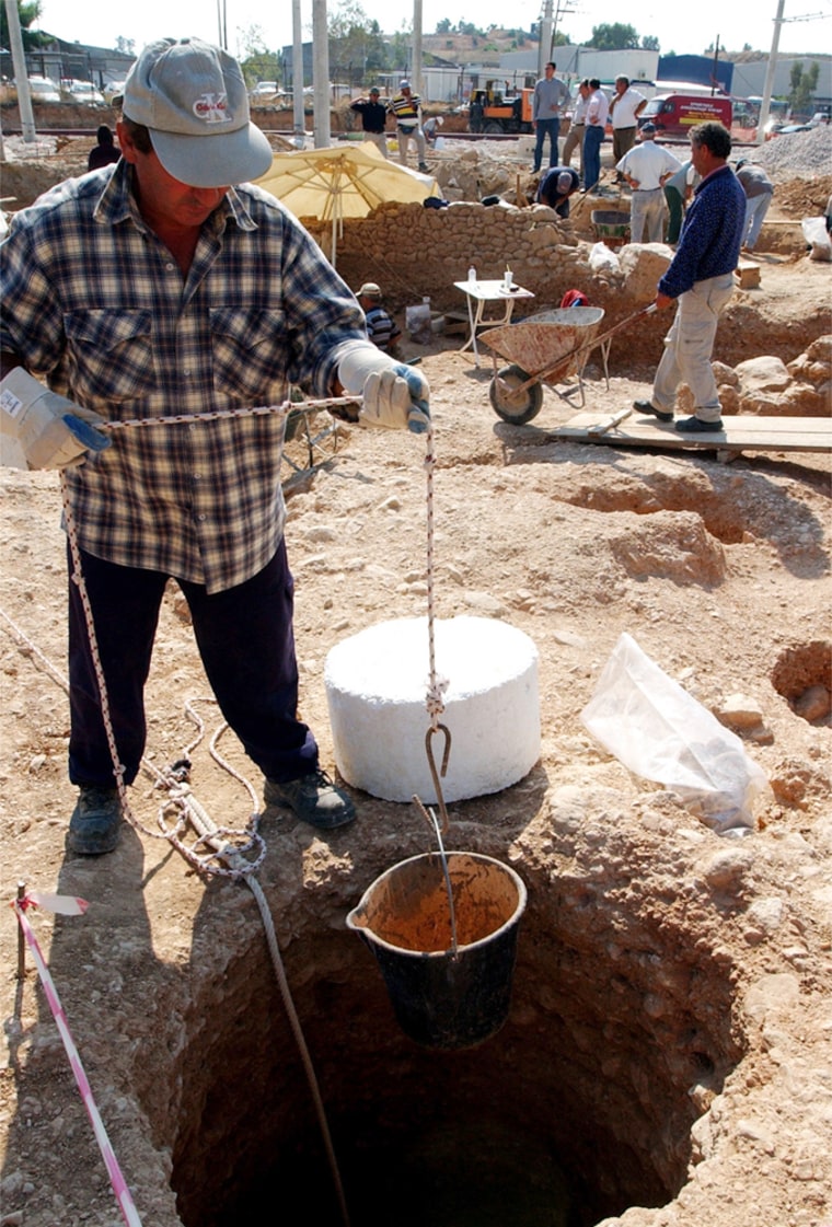 A worker lowers a bucket into a hole at the archaeological digging site at Hellenikon, Athens' former international airport.