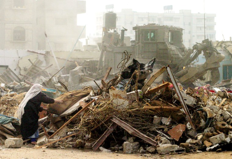 A Palestinian woman retrieves some of her belongings as an Israeli army bulldozer destroys her home next to the border with Egypt, in the Rafah refugee camp, southern Gaza Strip, Tuesday Jan. 20, 2004. Israeli army bulldozers flattened 30 houses and a mosque in this refugee camp Tuesday, Palestinian officials said. (AP Photo/Khalil Hamra)
