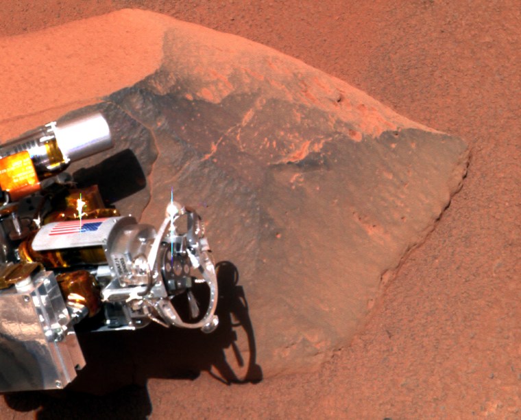A picture taken by Spirit's panoramic camera shows the rover's instrument-laden robotic arm next to the Martian rock nicknamed Adirondack. The rock abrasion tool, or RAT, sticks out toward the right, with an American flag visible on a plate.