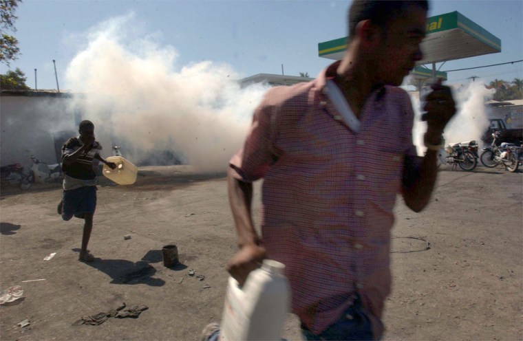People run through tear gas fired by rebels at a gas station in Gonaives, Haiti, Wednesday.