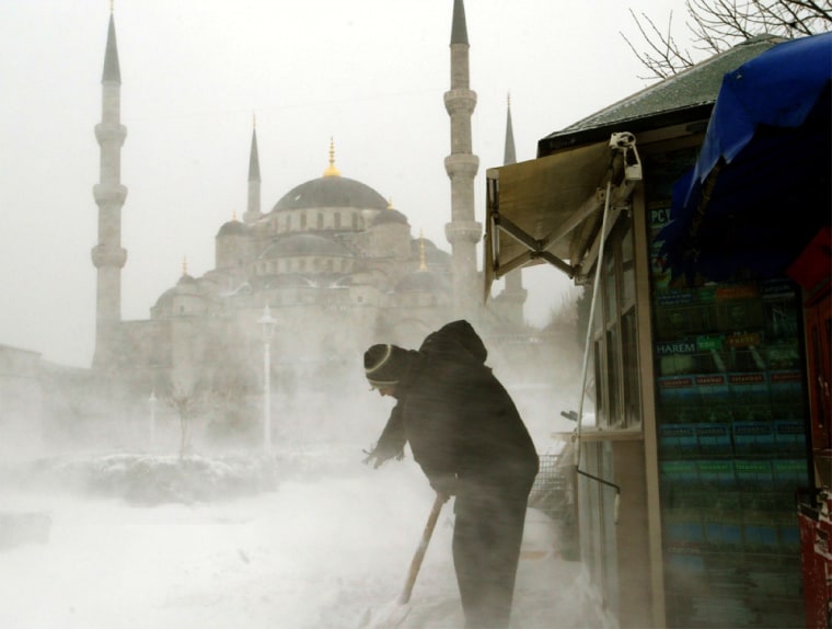 MAN SHOVELS SNOW IN FRONT OF HIS KIOSK NEAR THE BLUE MOSQUE IN ISTANBUL