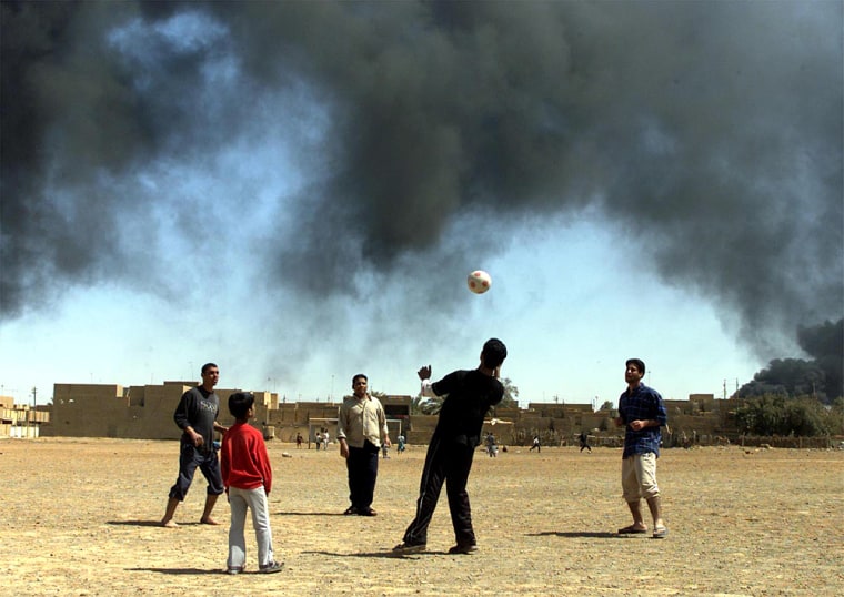 IRAQI BOYS PLAY SOCCER IN FRONT OF SMOKE FROM RAGING OIL FIRES IN BAGHDAD