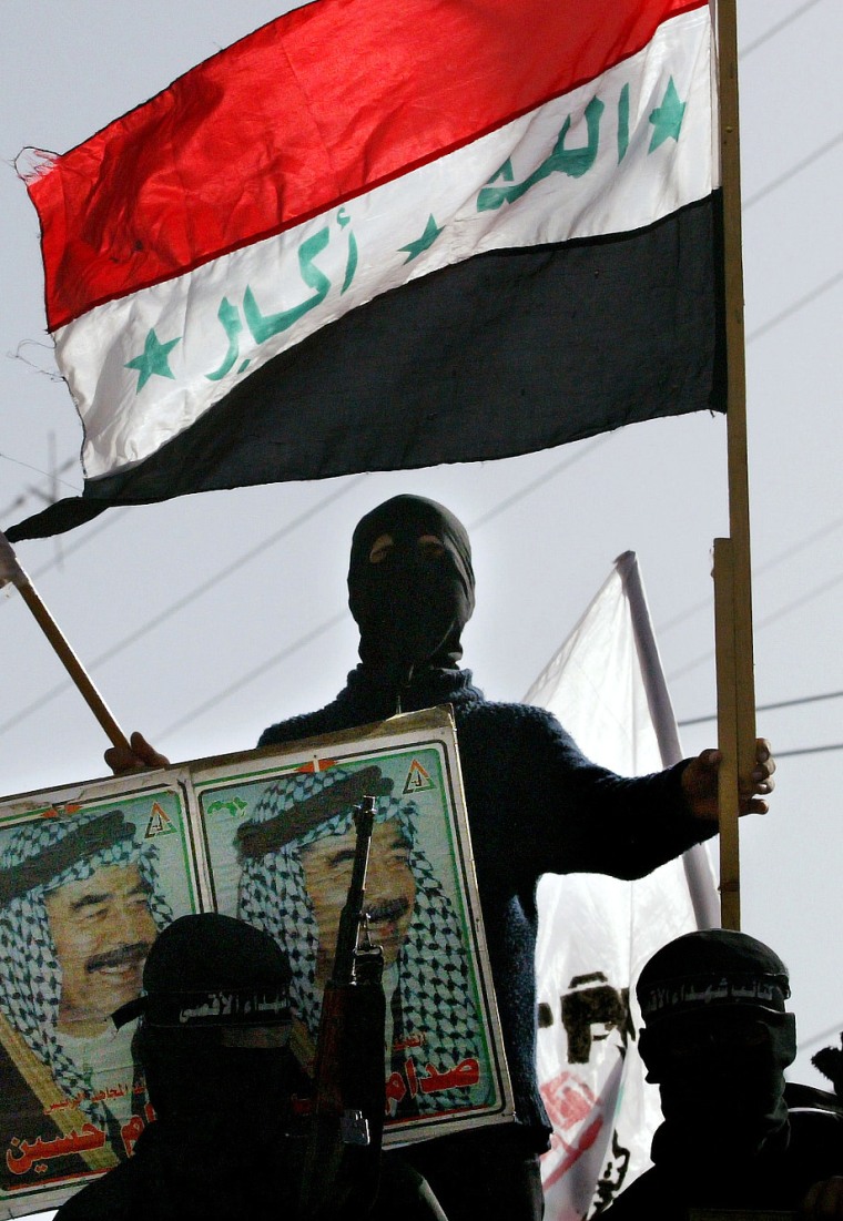 A masked militant from the Al Aqsa martyrs brigade holds the flag of Iraq, right, and the Palestinian flag, left, as others hold pictures of former Iraqi President Saddam Hussein during a small demonstration supporting the former Iraqi leader in the town of Khan Younis, in the southern Gaza Strip, Monday, Dec. 15, 2003. (AP Photo/Kevin Frayer)