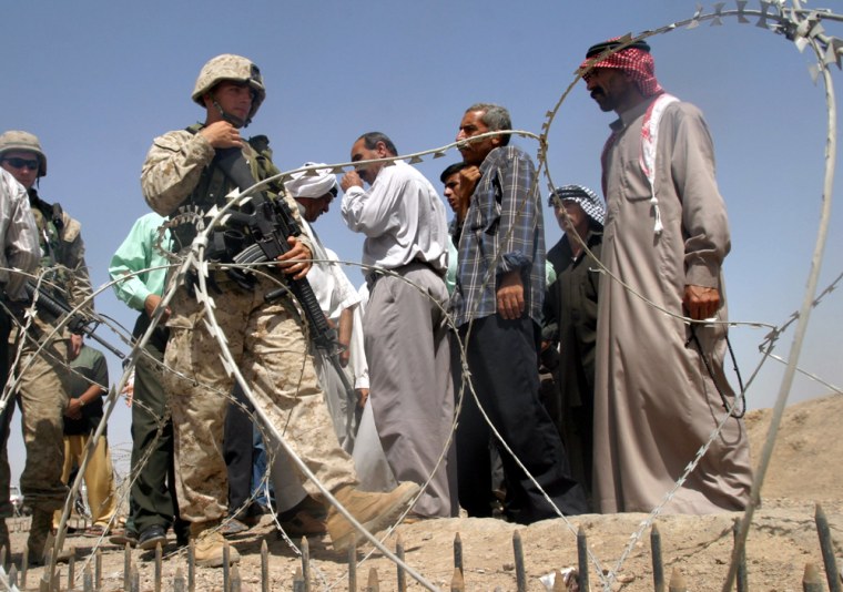 IRAQI MEN WALK PAST U.S. MARINES OUTSIDE THE ABU GHRAIB PRISON, WEST OF BAGHDAD