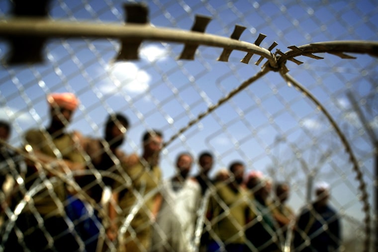 DETAINEES STAND BEHIND RAZOR WIRE AT ABU GHRAIB PRISON OUTSIDE BAGHDAD