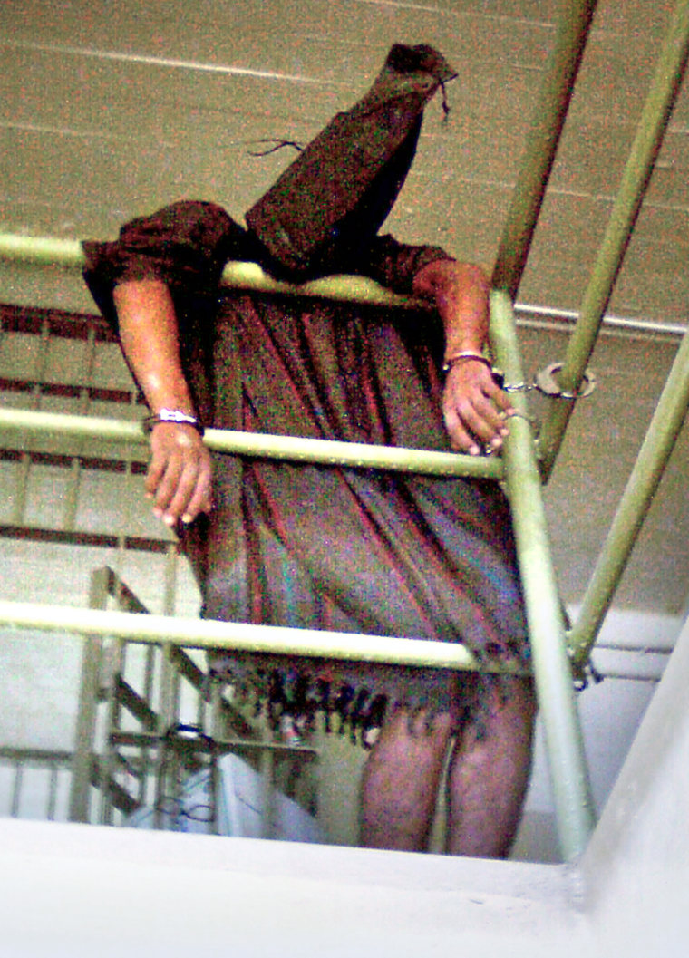  In this undated photo, a hooded Iraqi detainee appears to be cuffed at both wrists and collapsed over a rail at Abu Ghraib prison. 