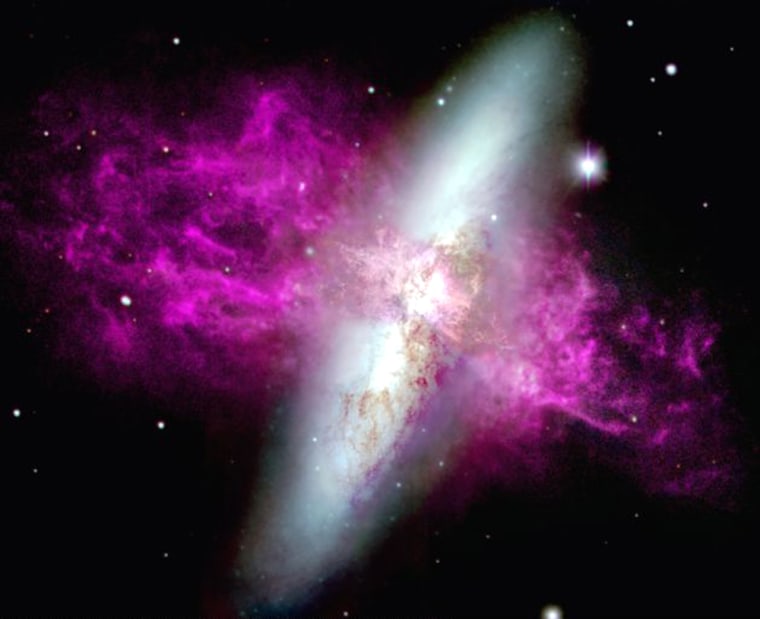 A color-coded image of the starburst galaxy M82 is oriented to show its supergalactic wind running left to right (north-south) and the nearly vertical disk of stars. Broad blue, green and red filters were used to render the relatively smooth stellar disk. Purple represents emission from hydrogen.