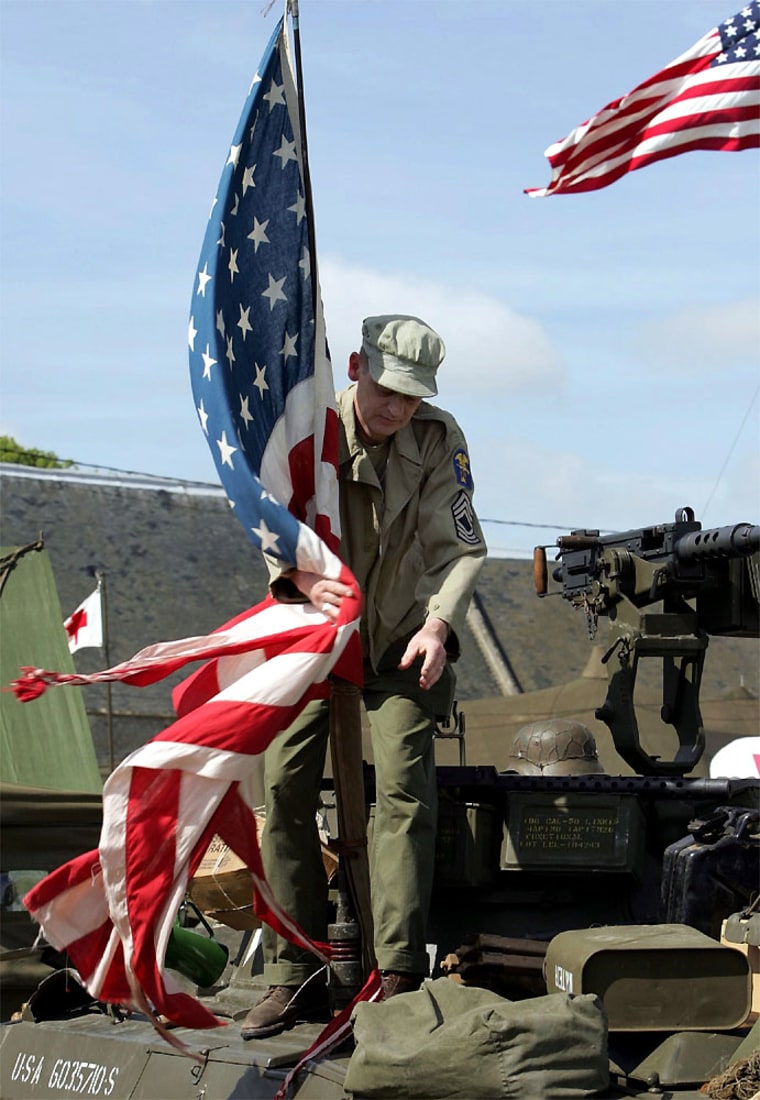 A FRENCH WW II HISTORY BUFF WRAPS THE US FLAG AROUND ITS MAST ON A VINTAGE TANK AT OMAHA BEACH