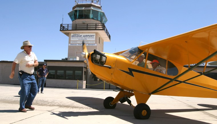 Pilot Dick Rutan (in orange hat) mans the controls of his 1939 Piper Cub J3 while a friend spins the propeller to start the engine at the Mojave Airport on Saturday. The airport was licensed as America's first inland spaceport on Thursday.