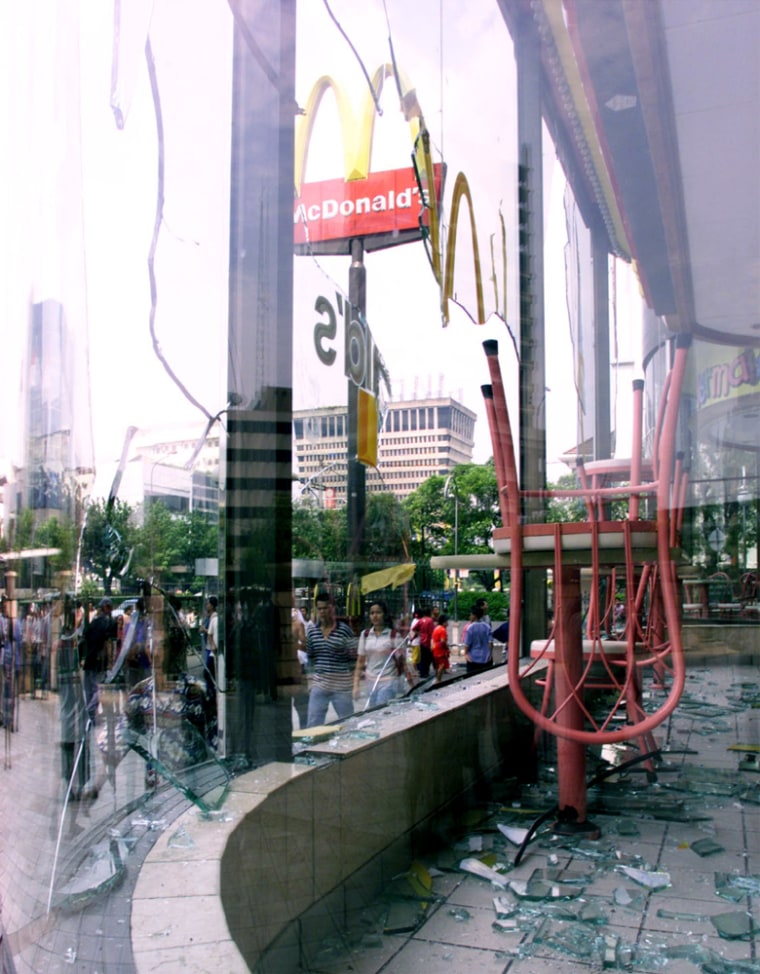 PASSERS-BY WALK PAST SMASHED WINDOWS OF A MCDONALDS RESTAURANT IN JAKARTA'S CHINATOWN