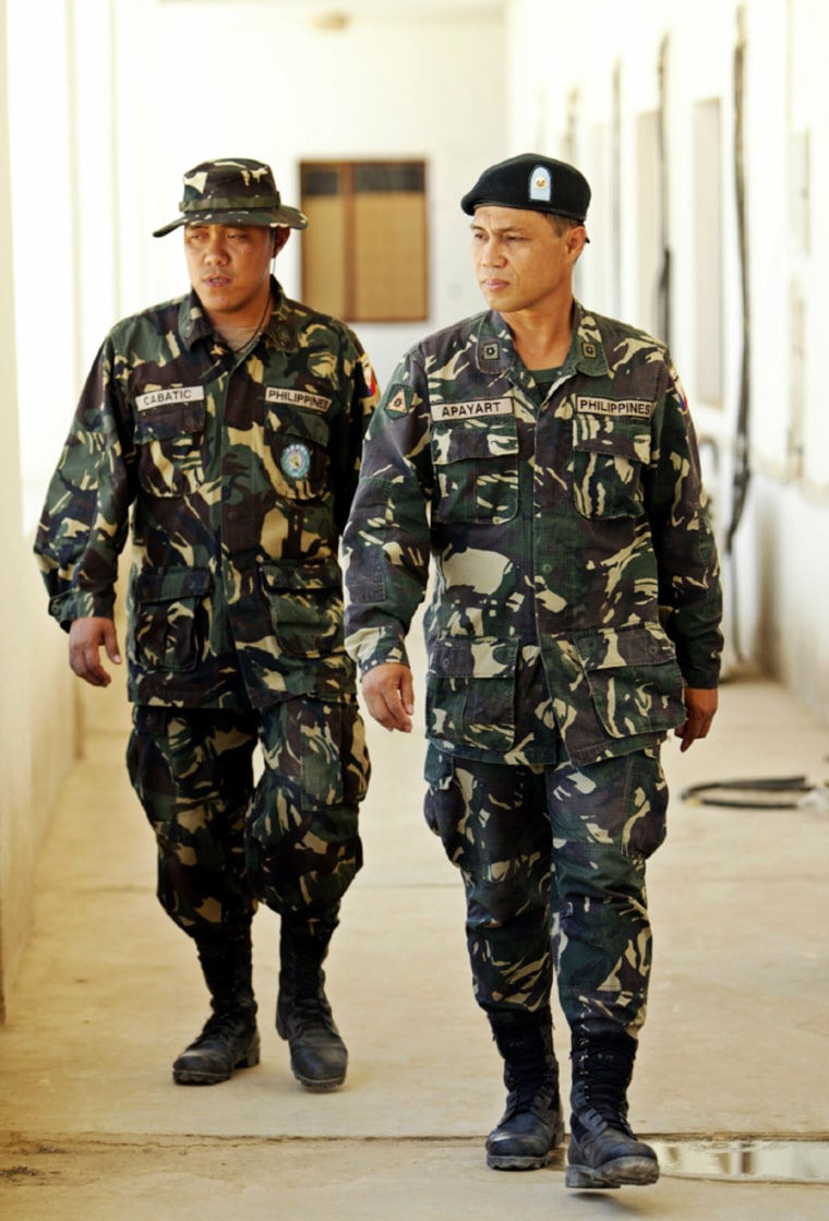 TWO PHILIPPINE ARMY SOLDIERS WALK THROUGH  A PASSAGEWAY AT THEIR MILITARY BASE IN HILLA