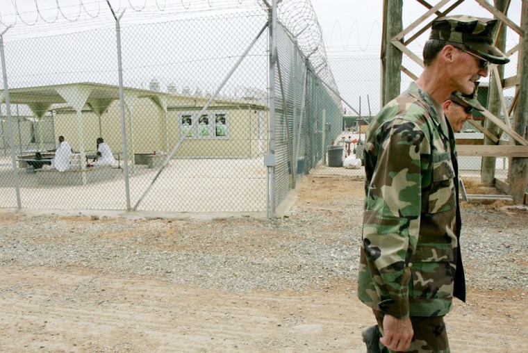 A U.S. Army soldier walks past detainees in a court yard at Camp Delta at Guantanamo Bay Naval Base, Monday, Aug. 23, 2004, in Cuba. On Tuesday, Aug. 24, preliminary hearings will begin for four suspected terrorists charged by the U.S. with war crimes as they appear before a commission of five military officers. (AP Photo/Mark Wilson, Pool)