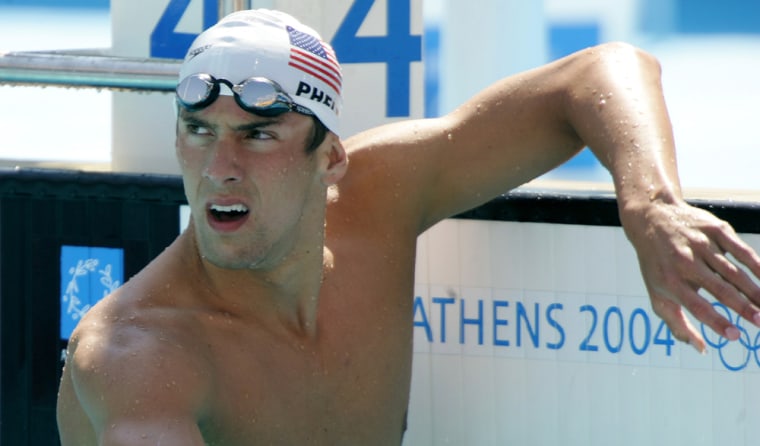 Michael Phelps of the US looks at the scoreboard after swimming his qualifying heat of the men 100 metres butterfly at the Athens 2004 Olympic Games