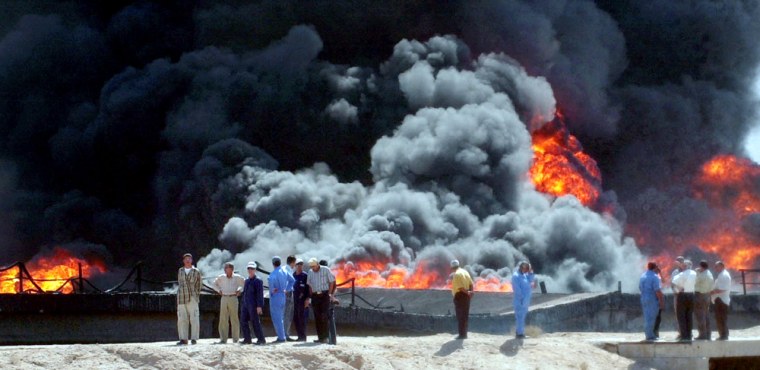 Foreign and Iraqi oil workers look on as flames and smoke engulf an oil pipeline in al-Barjisiya, southwest of Basra, Iraq, on Thursday. The pipeline was attacked on Wednesday.
