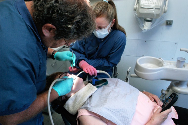 With a patient holding the remote control for a massaging chair, Steven Katz performs dental work at Smiles on Broadway in Malverne, N.Y.