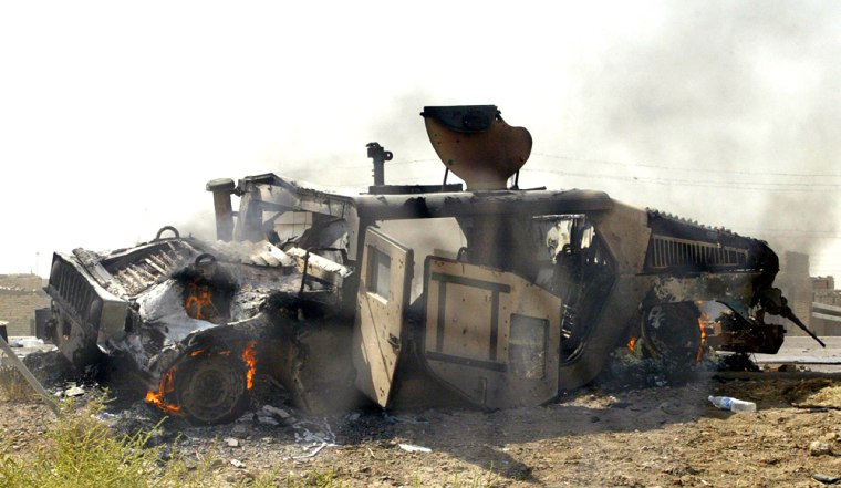 A burning US Humvee lies on the road aft
