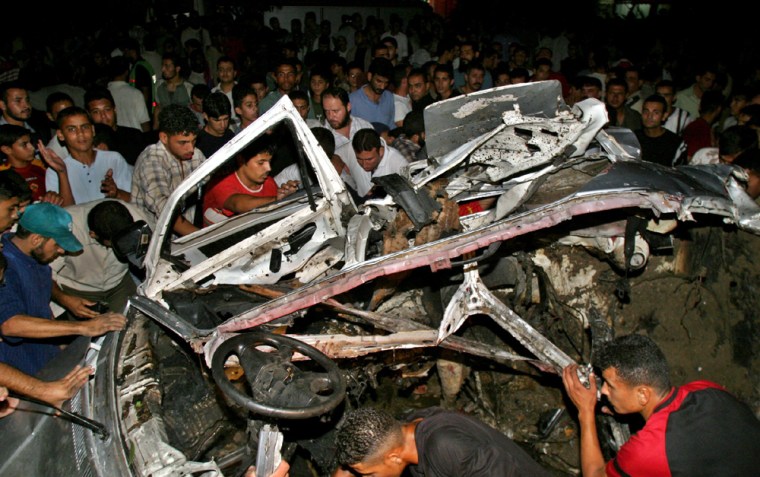 Palestinians surround a destroyed car after it was hit by a missile in Gaza