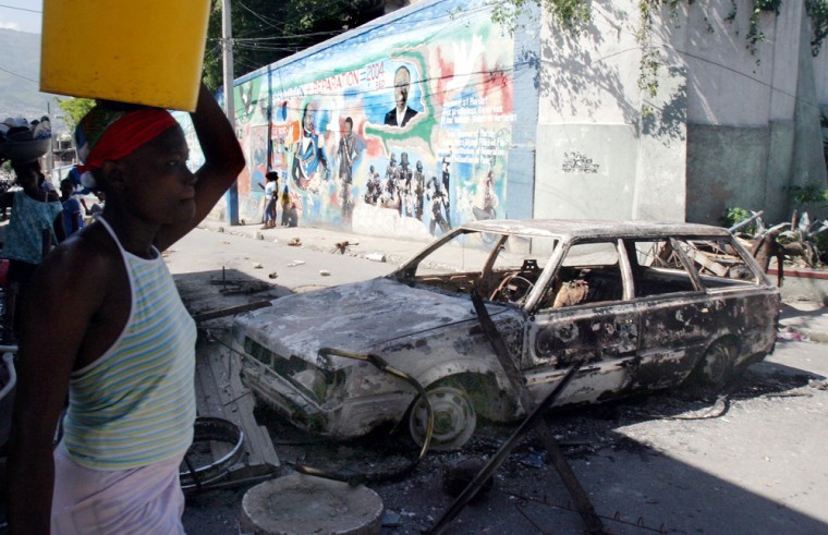 A pedestrian walks past a torched car used as barricade to block one of the main entrances to the pro-Jean-Bertrand Aristide slum of Bel-Air, in Port-au-Prince, on Monday.