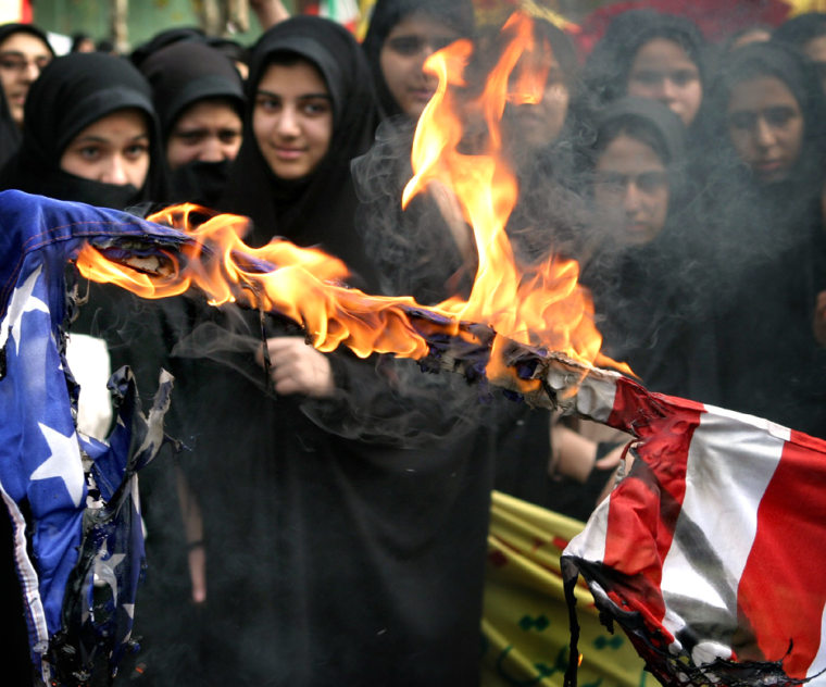 Iranian women stand behind a burning American flag in Tehran