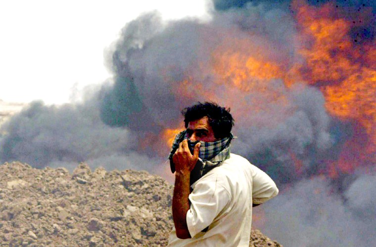 IRAQI MAN COVERS HIS FACE AS HE WATCHES A BURNING OIL PIPELINE NEAR BASRA