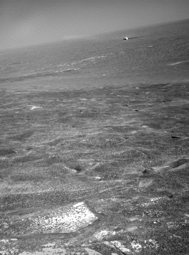 The Opportunity rover's heat shield shows up as a white speck in the distance, in an image that was captured by the rover's panoramic camera after rising out of Endurance Crater. Martian bedrock is visible in the foreground.