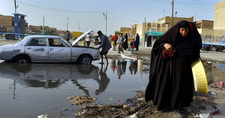 A woman walks past a man fixing his car in a flooded street in Baghdad's Shiite enclave of Sadr City last month.