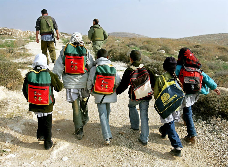 Israeli soldiers walk in front of Palestinian students from the Jundiyye family as they are escorted past the Havat Maon Jewish outpost settlement on their way home from school near the West Bank village of Tuwani.