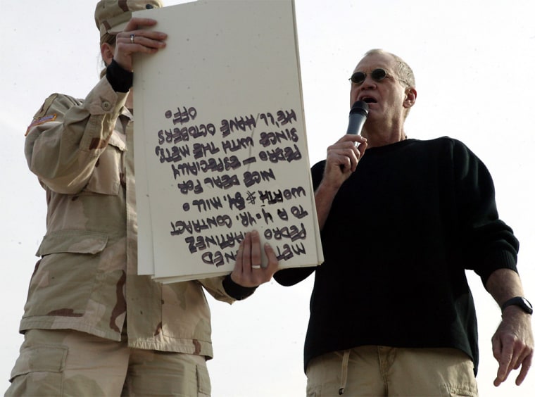 In this picture released by the U.S. Marines, an Army soldier holds up cue cards as comedian David Letterman delivers his opening monologue written specifically for the troops during \"The Late Show\" at Camp Taqaddum, Iraq, on Friday, Dec. 24, 2004. Letterman, along with his musical director Paul Shaffer and stage manager Biff Henderson, brought the popular late night television show to the Marines, sailors and soldiers currently stationed at Camp Taqaddum, Iraq. (AP Photo/U.S. Marines, Sgt. Luis R. Agostini)