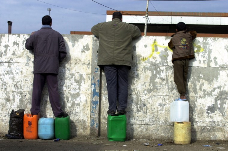 Iraqis look over a wall at a gas station while waiting to buy gasoline in Baghdad on Dec. 16.