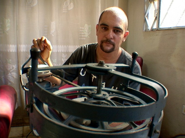 Oscar Millares sits in front of the industrial size food processor he is building from scrap metal and an old bicycle for his wife.