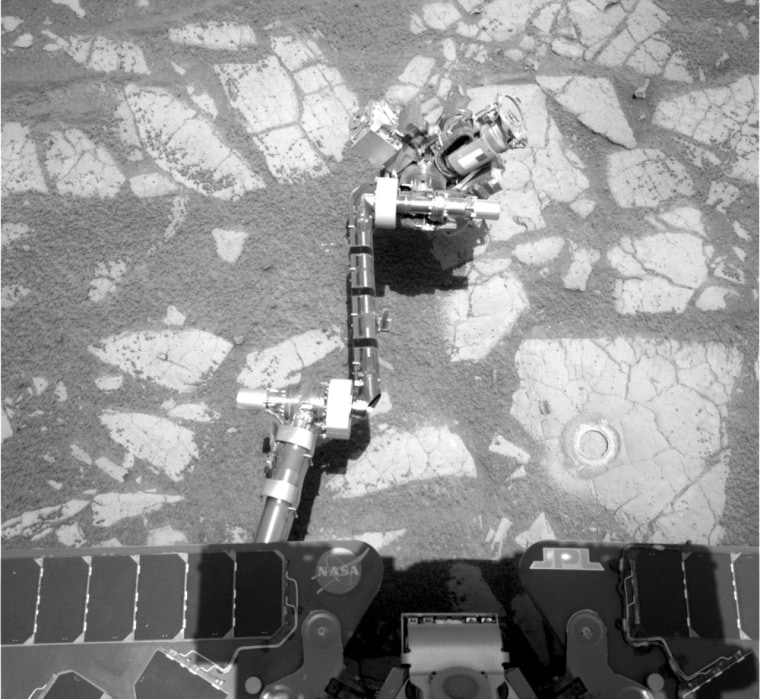 A picture snapped by the Opportunity rover's mast-mounted navigation camera shows its robotic arm stretched out to study Martian bedrock. The circle in one of the rocks is a hole drilled out by Opportunity's rock abrasion tool.